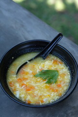 corn soup in a black bowl. sop jagung. sweet corn, chicken meat, carrots, celery, eggs, spices.