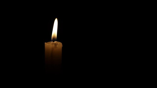 A candle flickers gently in the darkness, symbolizing grief and remembrance during a somber religious ceremony for lost loved ones, evoking deep sorrow and reflection.