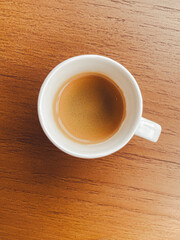 A close-up view of a white coffee cup filled with rich espresso, placed on a wooden table. A perfect scene for coffee lovers seeking warmth and comfort..