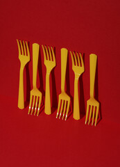 Yellow Plastic forks on red background with shadow. Minimalism. Creative layout. Food concept