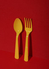 Yellow Plastic spoon and fork on red background with shadow. Minimalism. Creative layout. Food concept