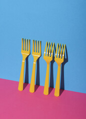 Yellow Plastic forks on pink blue background with shadow. Minimalism. Creative layout. Food concept