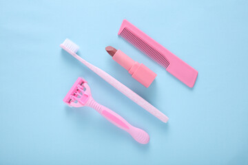 Personal hygiene items. Pink Toothbrush with razor and comb, lipstick on blue background. Top view
