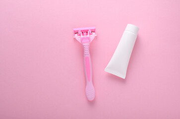 Razor with cream tube on pink background
