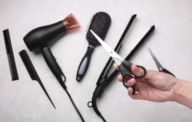 Naklejka premium Hand holding scissors among hairdressing tools on grey background