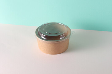 Cardboard round food box with plastic lid on table, turquoise background