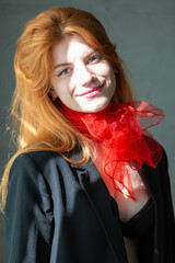 Portrait of a red-haired girl with a red scarf around her neck, in a suit and top, soft morning light from the blinds.