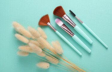 Makeup brushes with lagurus flowers on mint green background. Top view. Beauty concept