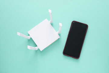 Modern four-antenna Wi-Fi router and smartphone on mint green background. Top view