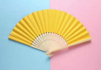 Traditional yellow Asian hand fan on pink blue background