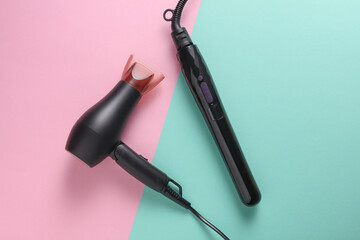 Modern black hair dryer and hair iron on pink blue background