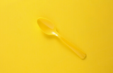 Plastic spoon on yellow background close up