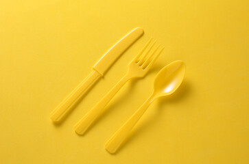 Plastic fork, spoon and knife on yellow background