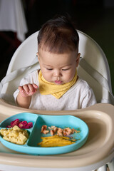 9 month old Asian baby boy is learning to eat, with food on the table, the baby eats and commands himself, it seems a bit messy