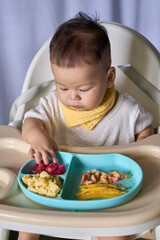 9 month old Asian baby boy is learning to eat, with food on the table, the baby eats and commands himself, it seems a bit messy