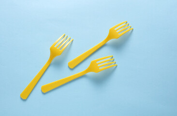 Many Yellow Plastic forks on blue background. Top view