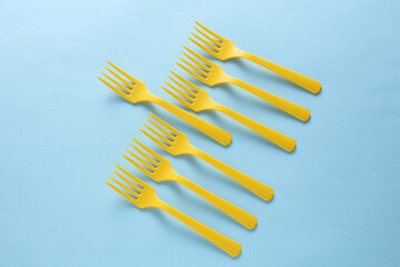 Many Yellow Plastic forks on blue background. Top view