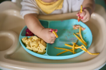 9 month old Asian baby boy is learning to eat, with food on the table, the baby eats and commands himself, it seems a bit messy