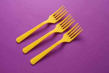 Yellow Plastic forks on purple background.