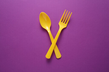 Yellow Plastic fork and spoon on purple background.