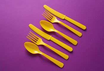 Yellow Plastic forks, knives and spoons on purple background