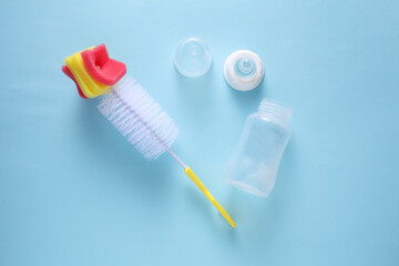 Newborn feeding bottle and washing brush on blue background. Top view