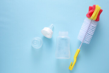 Newborn feeding bottle and washing brush on blue background. Top view
