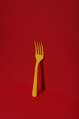 Yellow Plastic fork on red background with shadow. Minimalism. Creative layout. Food concept