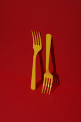 Yellow Plastic forks on red background with shadow. Minimalism. Creative layout. Food concept