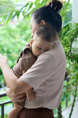 Mother is playing with her 9-month-old son in the summer, in a cool, green setting.
The mother and daughter wore coffee brown clothes. Both are Asian.