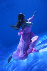 Fototapeta premium Woman in pink dress dancing underwater in the pool in blue light
