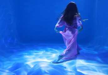 Woman in pink dress dancing underwater in the pool in blue light