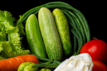 arrangement of vegetables commonly used in indonesian dishes, including tomatoes, carrot, cucumbers, long beans, pumpkin, cabbage, and lettuce. Put on traditional bamboo basket, solid black background
