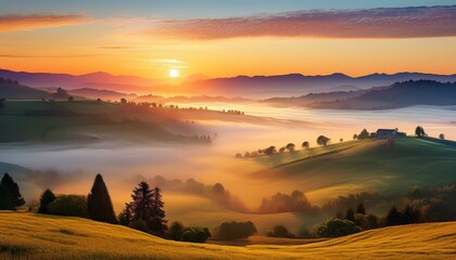 Obraz premium Distant sunrise over a misty valley A panoramic view of a misty valley at sunrise. Mist rolls gently over the hills and fields