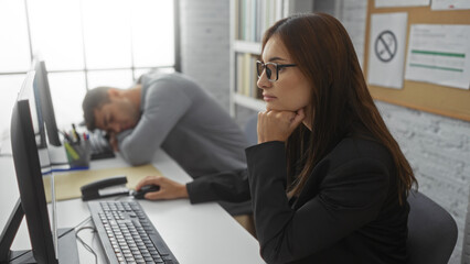 Woman working on desktop computer in office while man sleeps beside in living room with bright daylight coming through window.