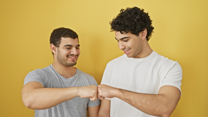 Two smiling men fist bumping in a friendly gesture against a vibrant yellow background, showcasing camaraderie.
