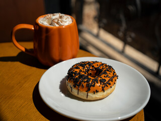 Autumn pumpkin spice latte in an orange pumpkin mug with a whipped cream and cinnamon, orange glazed donut 