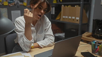 A surprised young woman examines evidence on her laptop in a cluttered detective's office