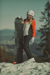  A girl with a snowboard in her hands against the backdrop of snowy mountains