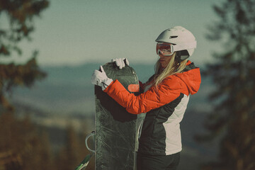  A girl with a snowboard in her hands against the backdrop of snowy mountains
