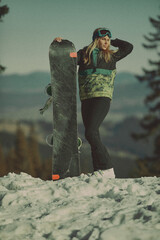  A girl with a snowboard in her hands against the backdrop of snowy mountains