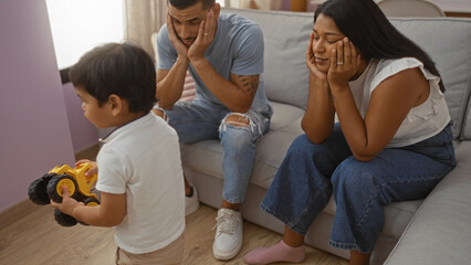 Latin family of man, woman, and child feeling bored in a living room, with parents sitting on a...