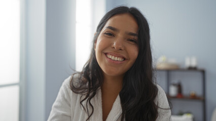 Young woman smiling in a wellness center wearing a robe, exuding beauty and calm in an indoor spa...