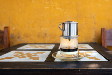 Glass of traditional hot Vietnamese coffee with condensed milk on wooden table in cafe in Vietnam..