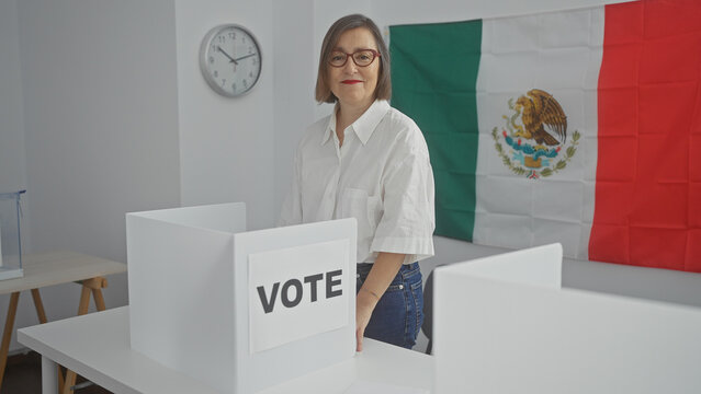 Middle-aged woman votes indoors with mexican flag in background, symbolizing democracy.