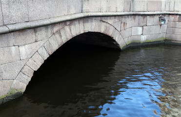 granite arch of the bridge with a black opening over the blue water of the canal