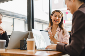 young woman smiles while engaging in conversation with colleagues at modern office setting. atmosphere is collaborative and friendly, with laptops and coffee cups on table