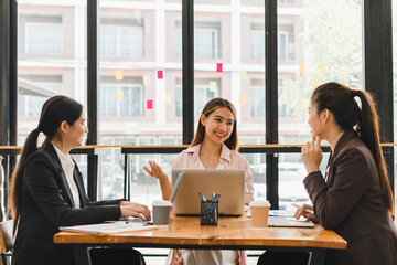 Collaborative business meeting with three women discussing ideas at modern office table. They are engaged and smiling, showcasing teamwork and communication