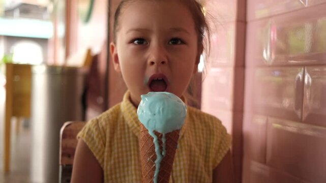 Portrait little girl looks and bite cold ice cream in a waffle cone