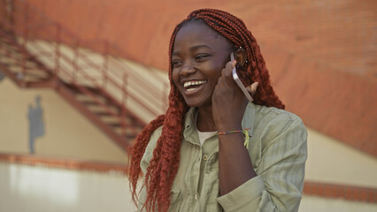 A young african american woman enjoys a conversation on a smartphone in a sunny urban street...
